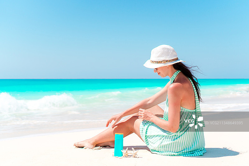一个年轻漂亮的女人拿着防晒霜躺在沙滩上图片素材