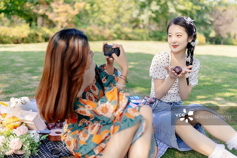 两个亚洲青年美女闺蜜在户外野餐垫上野餐用数码相机给对方拍照图片素材