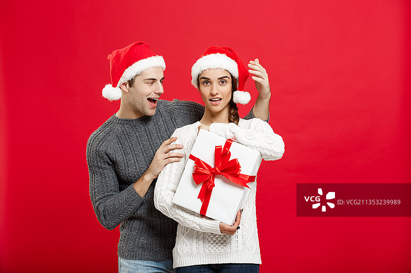 在红色背景下，微笑的情侣拿着礼品盒图片素材