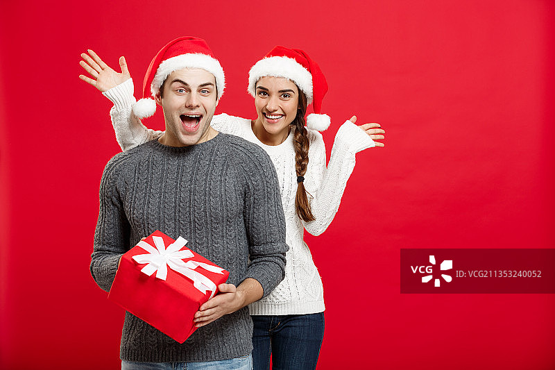 红色背景下，微笑的年轻夫妇拿着礼品盒的肖像图片素材