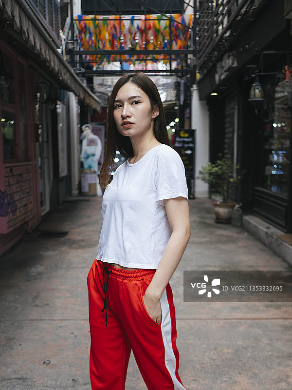 时尚肖像-美丽的亚洲年轻女子在白衬衫和红色运动裤摆姿势在街道小巷。图片素材