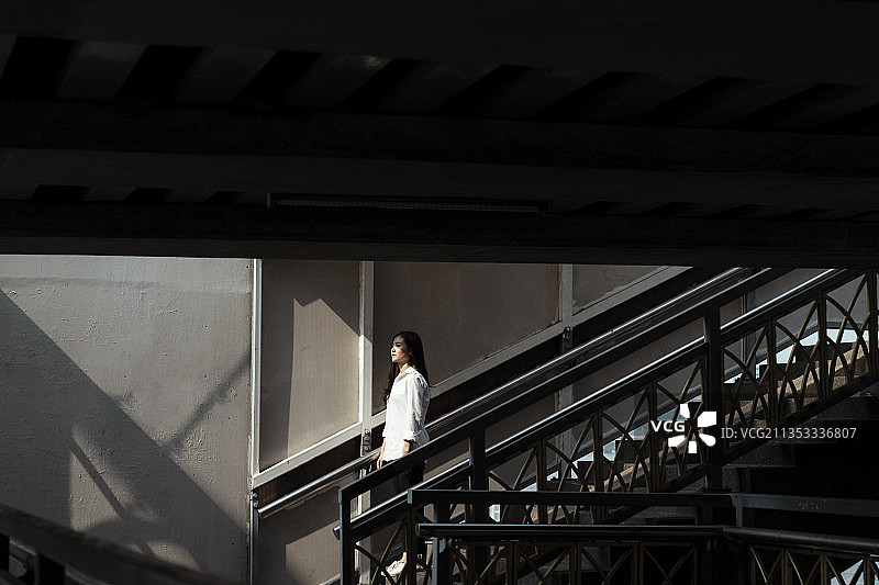 一个女人走下桥的楼梯，走向夏日的阳光，直视着阳光。图片素材