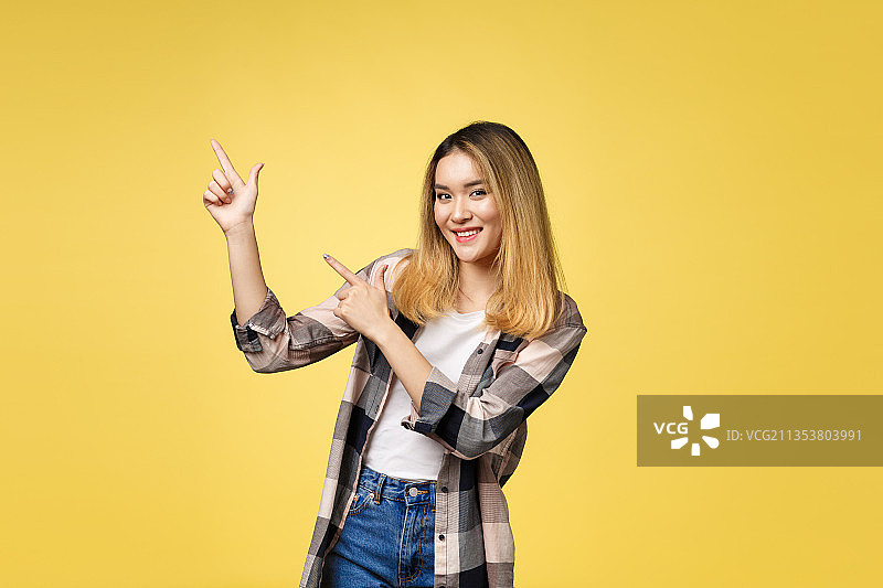 微笑的年轻女子肖像，站在黄色的背景下做手势图片素材