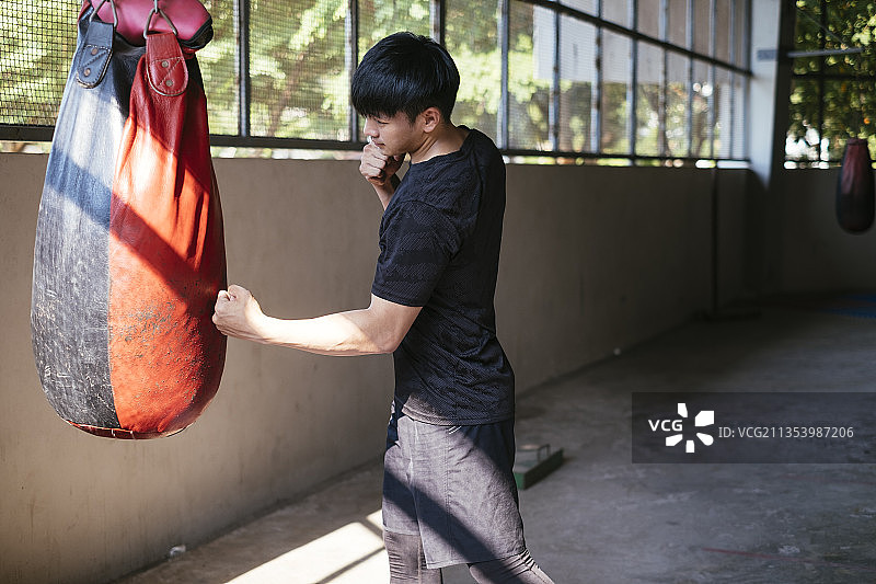 运动亚洲泰国人在黑色运动服练习泰拳沙袋。拳击和踢。图片素材