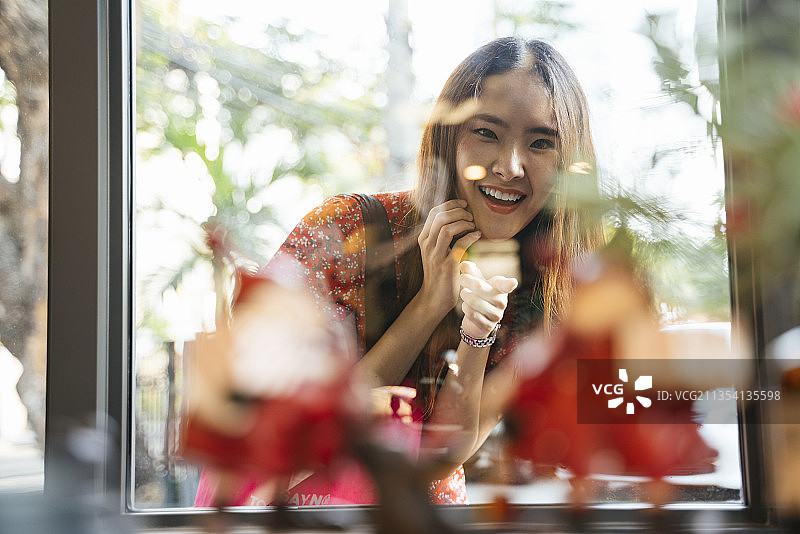 年轻的亚洲女人穿着红色的衣服在街上的购物窗口后面看着东西，带着愉快的表情。图片素材
