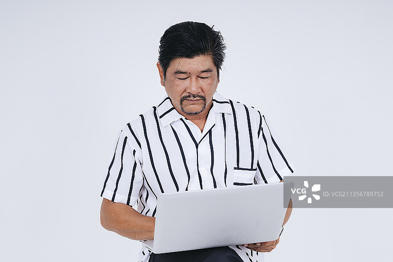 老年老人的肖像在白色的背景上使用笔记本电脑隔离白领衬衫。图片素材