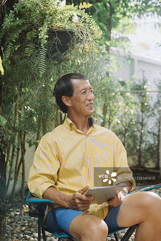 一位亚洲长者在公园里用数码笔记本电脑，穿着黄色t恤。图片素材