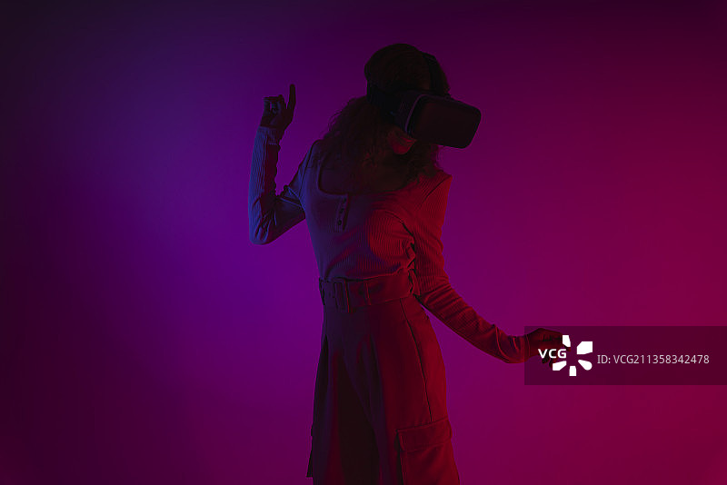 快乐女人在霓虹灯背景下戴着虚拟现实VR眼镜。图片素材