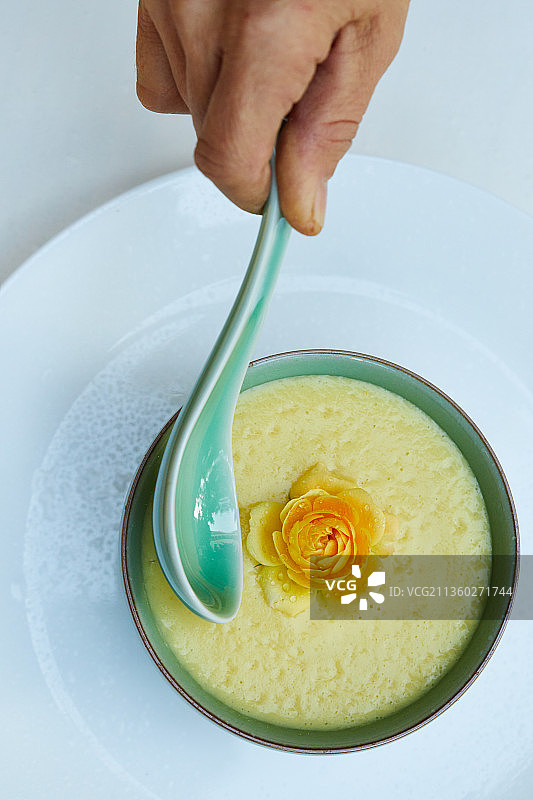 花园里白色餐桌上的一碗有黄色花朵的有机素食玉米羹图片素材