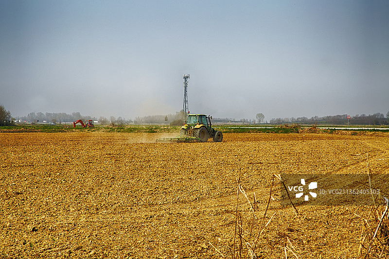 拖拉机在田野里工作，天空映衬下的农田风景图片素材