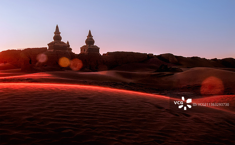 日出时分，太阳光映红了黑城遗址，并在遗址外围的沙漠上画上了一抹红色的弧线。图片素材
