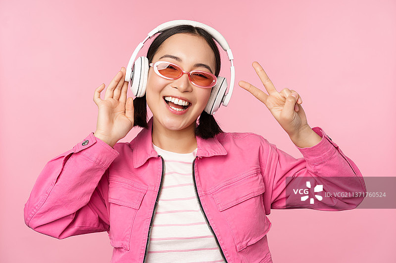 跳舞时尚的亚洲女孩听音乐在耳机里，摆姿势图片素材