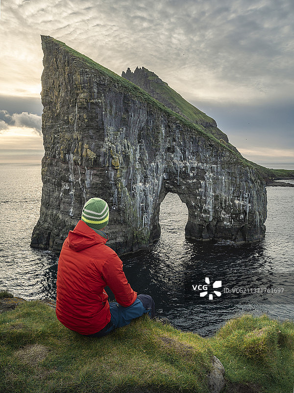 日落时分，一个人坐在法罗群岛的德兰加尼尔岩石前图片素材