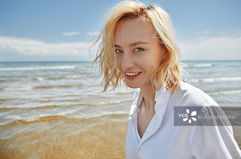 金发碧眼，无忧无虑的女人，穿着白衬衫，在海边玩耍图片素材