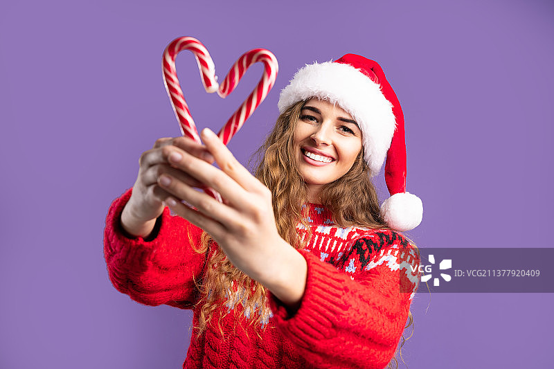 快乐的年轻女人戴着圣诞老人的帽子，用糖果做成紫色的心图片素材