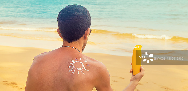 一个男人在沙滩上，背上涂着防晒霜选择性聚焦图片素材