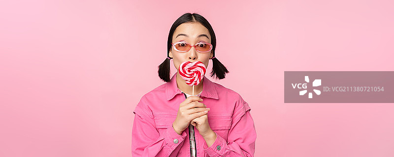 时尚的韩国女孩舔棒棒糖，吃糖果和微笑图片素材