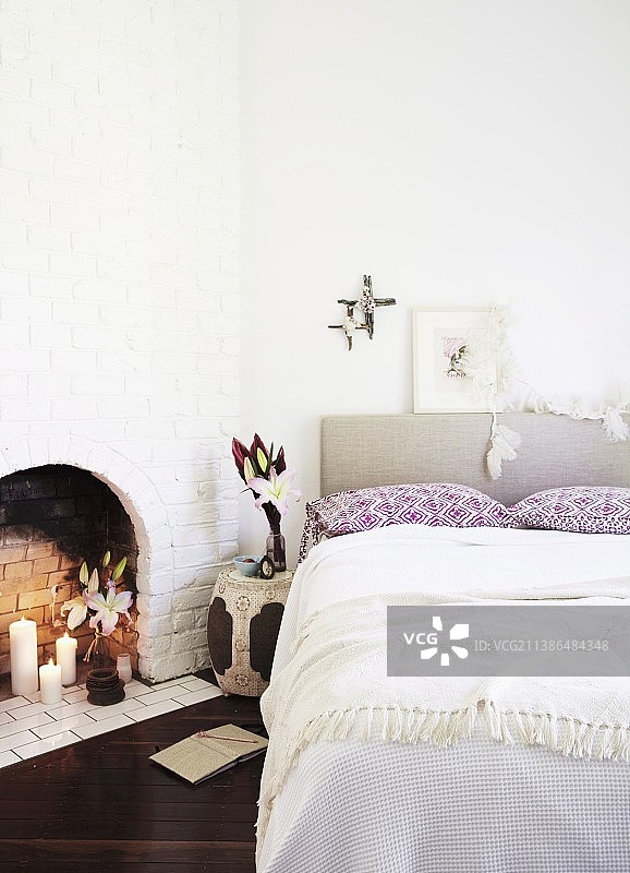 双人床上有软垫床头板，旁边是白色砖墙里的开放式壁炉图片素材