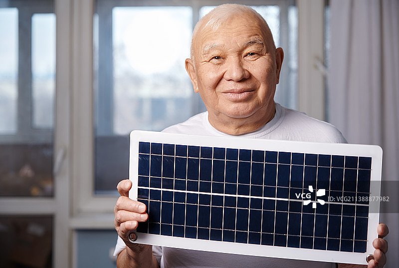 老人在家里拿着太阳能电池板。可再生可持续能源概念图片素材