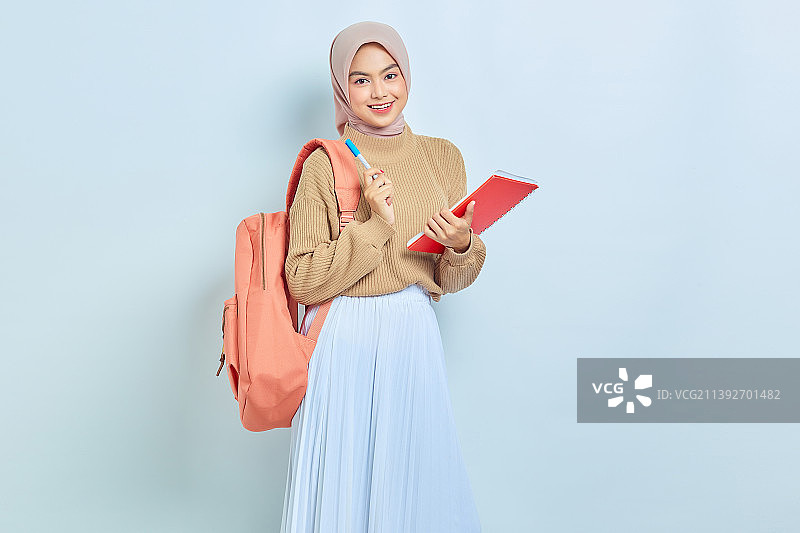 微笑的年轻亚洲穆斯林女学生在棕色毛衣和背包里拿着书和笔图片素材