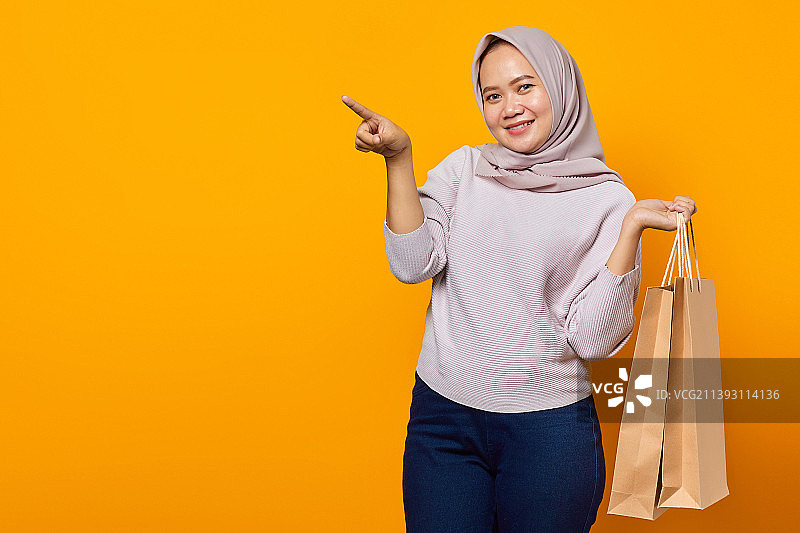 印度尼西亚，兴奋的亚洲女人拿着购物袋指着空的地方的肖像图片素材