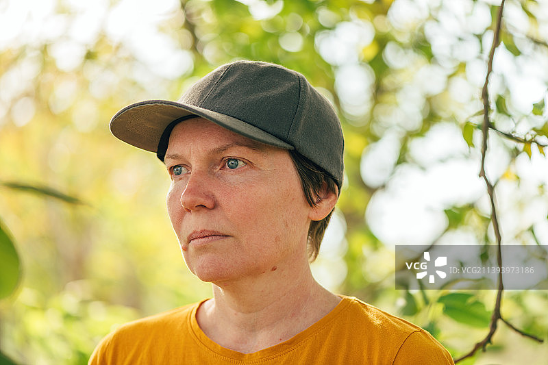 在塞尔维亚的核桃树果园里，穿着橙色t恤和卡车司机帽子的女性农场工人肖像图片素材