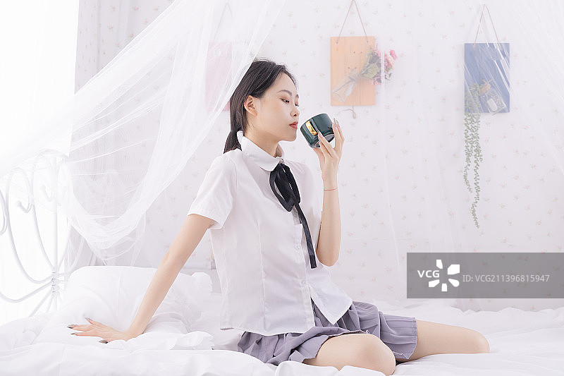 年轻女子坐在家里的床上喝水图片素材