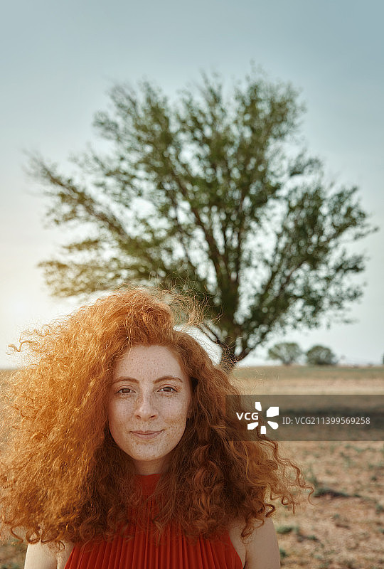 年轻的红发女子的肖像与长长的卷发户外一棵树。很适合做书的封面图片素材