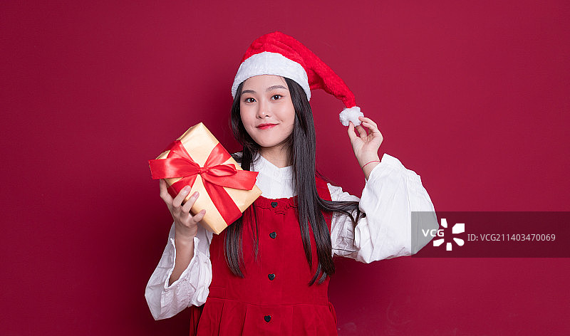 红色背景前带着圣诞帽拿着礼物的年轻女孩图片素材