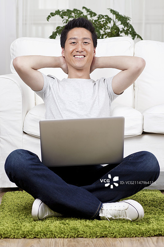 一个坐在绿色地毯上用笔记本电脑的青年男士图片素材