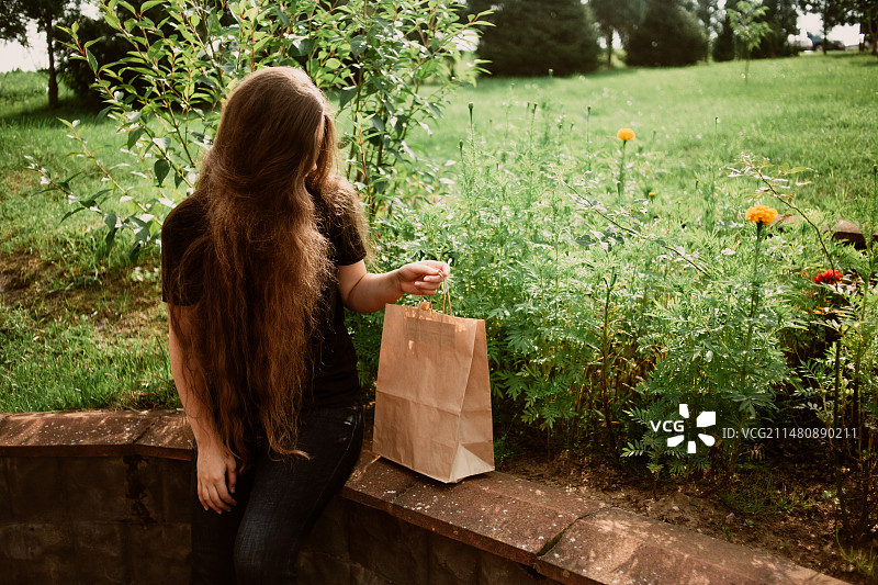 白俄罗斯，年轻女子拿着购物袋坐在植物旁图片素材