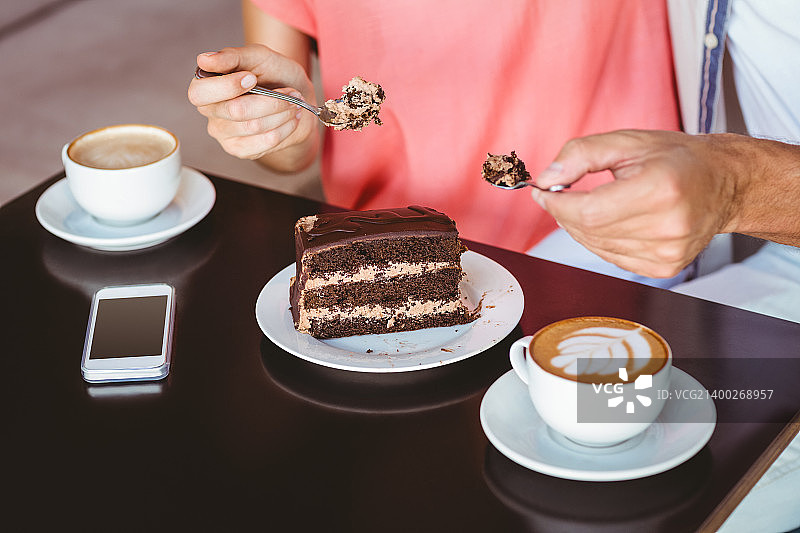 一对可爱的情侣在咖啡馆里分享一块巧克力蛋糕图片素材