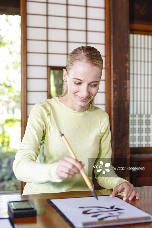 一个白人妇女在传统的日本房子里练习书法图片素材