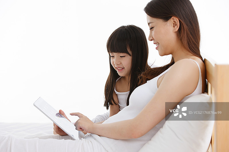 母亲和女儿在床上使用平板电脑图片素材