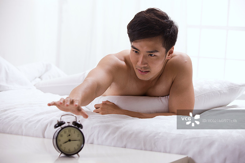 年轻男人趴在床上拿闹钟图片素材