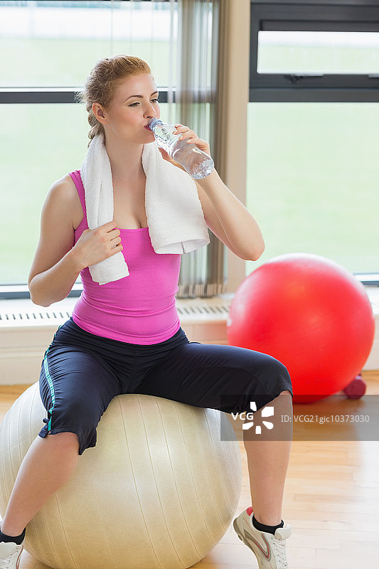 健身房里坐着健身球，喝着水的年轻美女图片素材