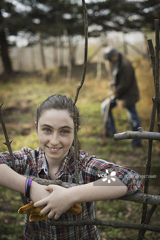 有机农场上，一个小女孩靠在篱笆上。一个男人在后面挖土。图片素材