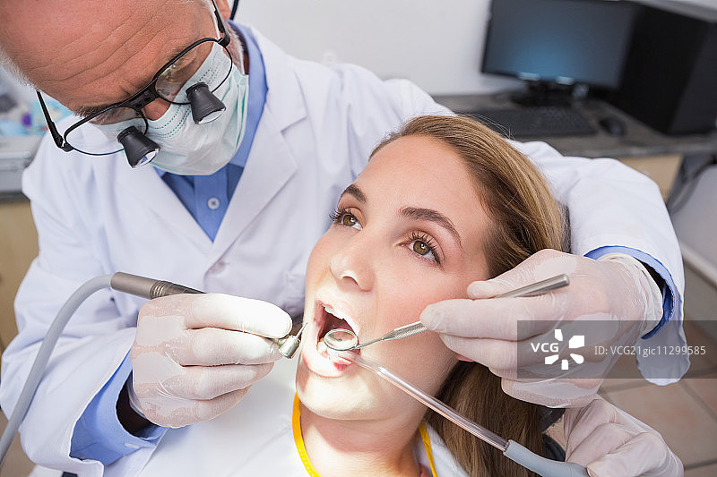 牙科医生和助手在牙科诊所的牙医椅上检查病人的牙齿图片素材