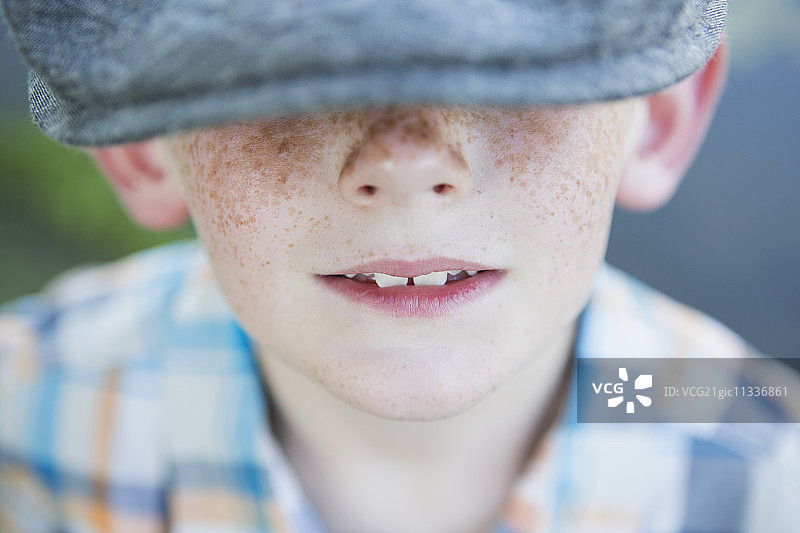 一个长着雀斑鼻子的小男孩，戴着一顶大帽檐的帽子。图片素材