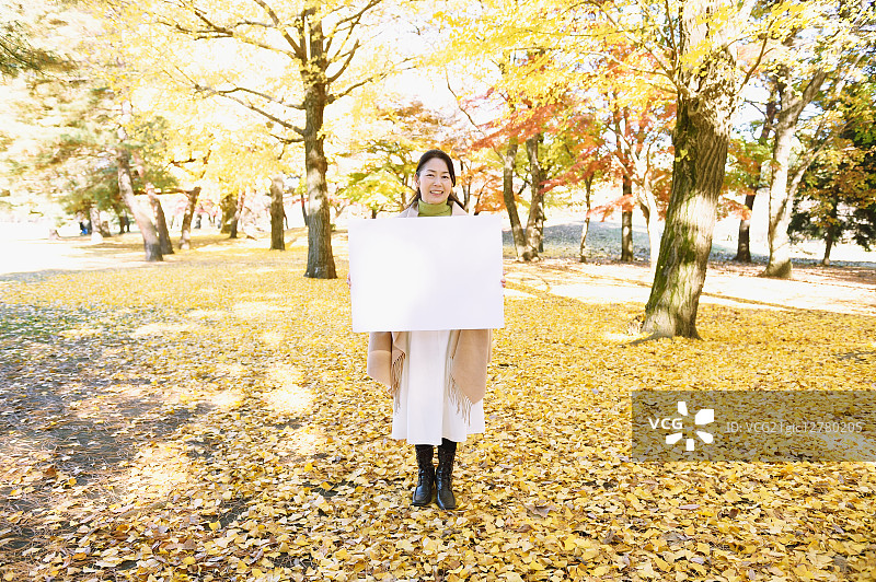 秋天，在城市公园里，一位年长的日本妇女拿着白板图片素材