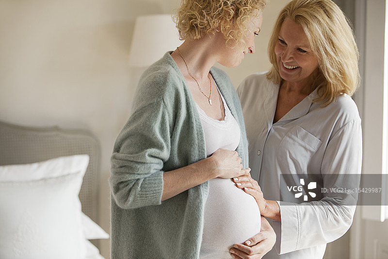 母亲微笑着抚摸着怀孕的女儿的肚子图片素材