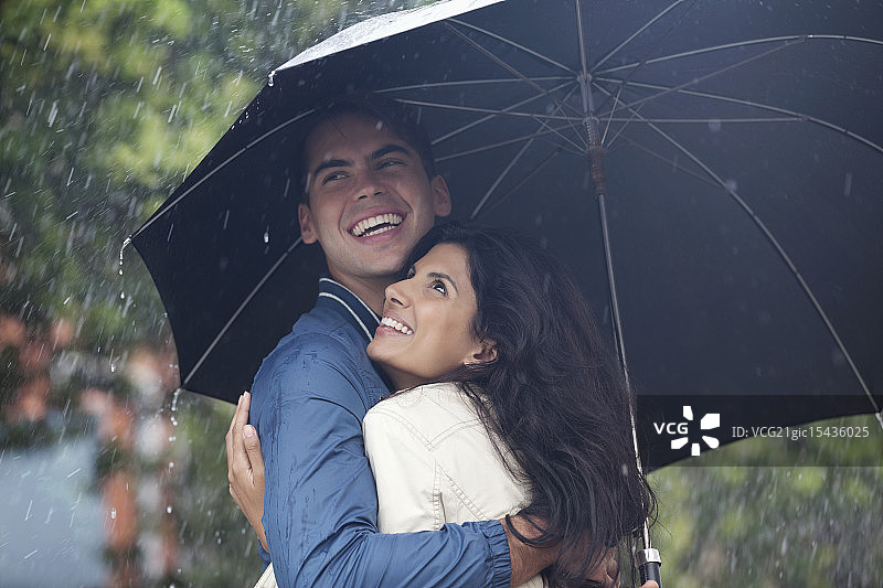幸福的情侣在雨中的雨伞下拥抱图片素材