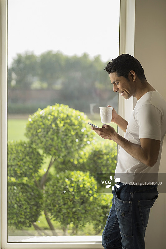 印度，男人在窗口拿着咖啡杯和手机图片素材