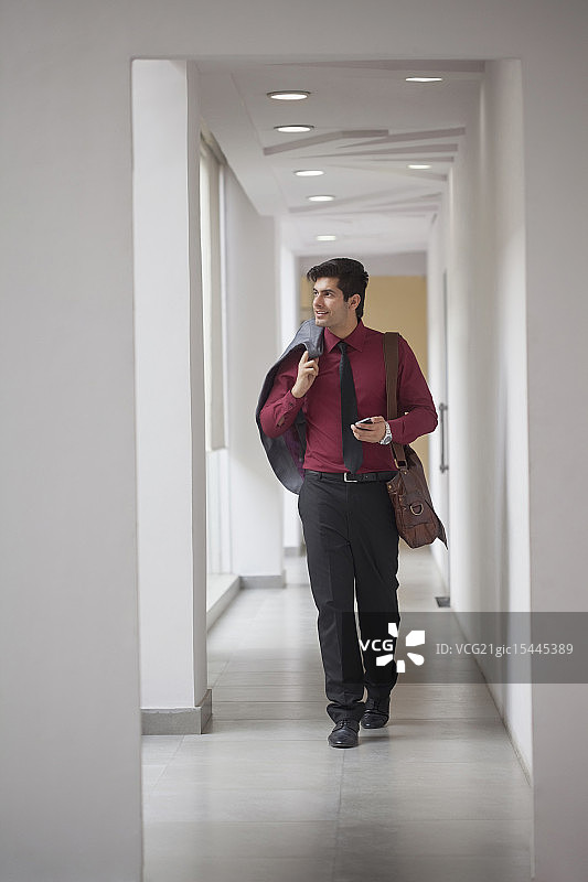 印度，一个男人肩上扛着夹克，手里拿着电话走在走廊上图片素材