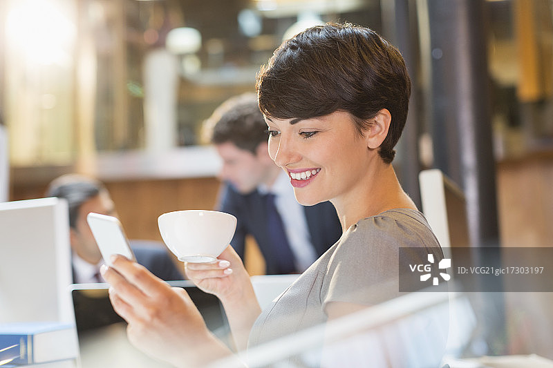 女商人在办公室喝咖啡，用手机发短信图片素材