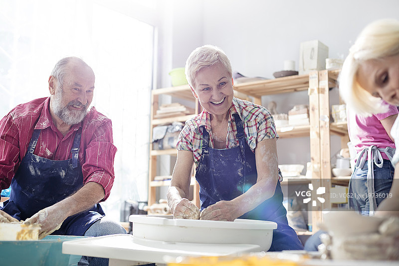 一对微笑的老年夫妇在工作室里用陶轮图片素材