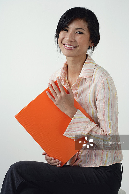 一位女士拿着一个橙色的文件夹，对着镜头微笑图片素材