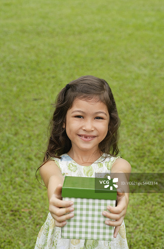 女孩站在草地上，拿着礼盒对着相机图片素材