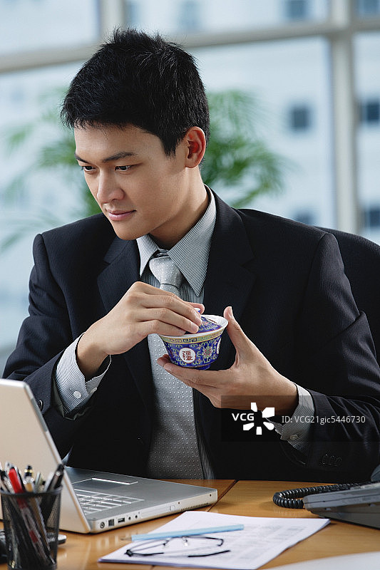 一名男子坐在他的办公桌前，手里拿着一个中国茶杯图片素材