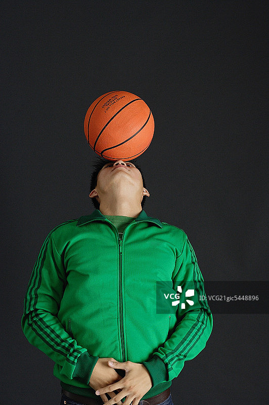 穿着绿色夹克的年轻人用鼻子平衡篮球图片素材
